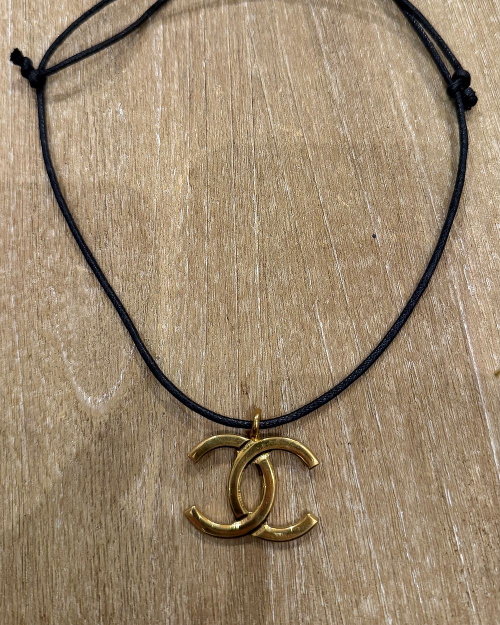 Interlock Pendant on cord, flat lay on oak — Maison Dorée vintage charm necklace