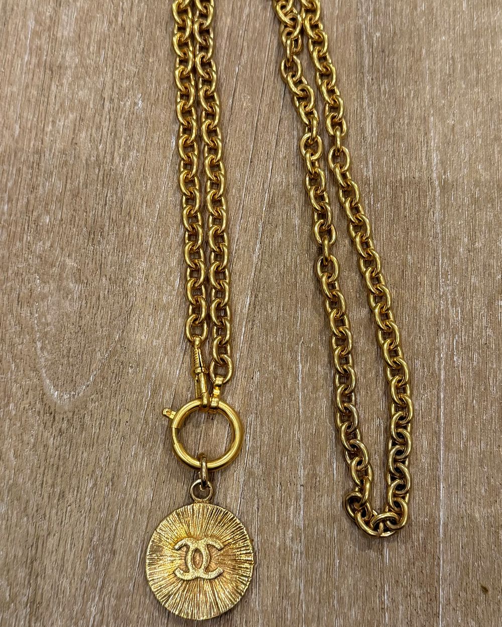 Sunburst on chain, flat lay on oak — Maison Dorée vintage charm necklace