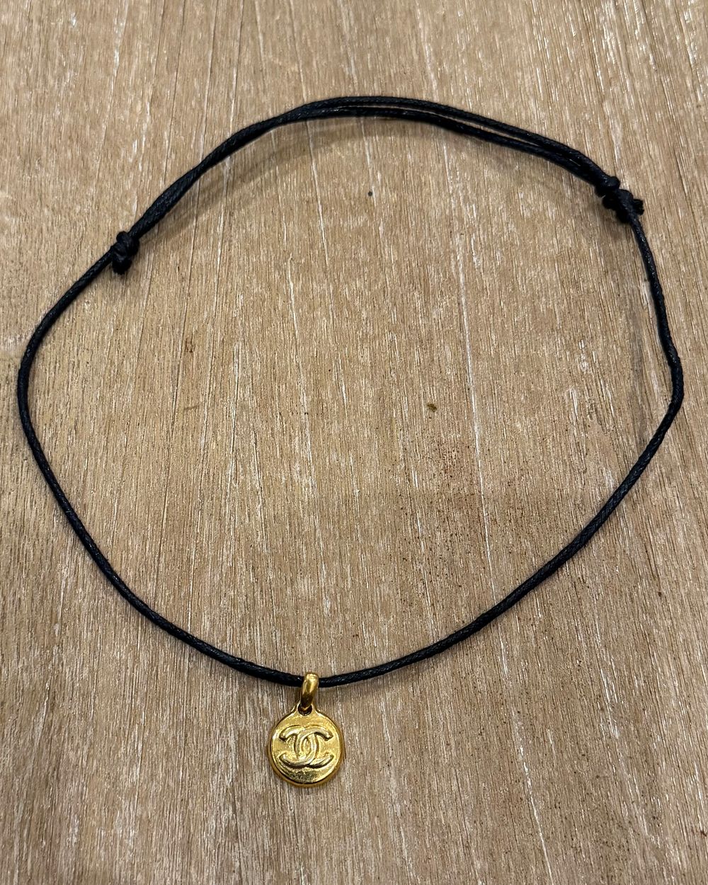 Petite Coin on cord, flat lay on oak — Maison Dorée vintage charm necklace
