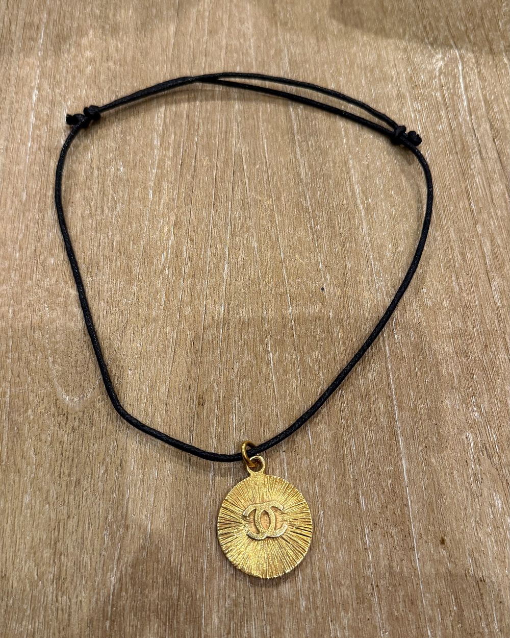 Sunburst on cord, flat lay on oak — Maison Dorée vintage charm necklace